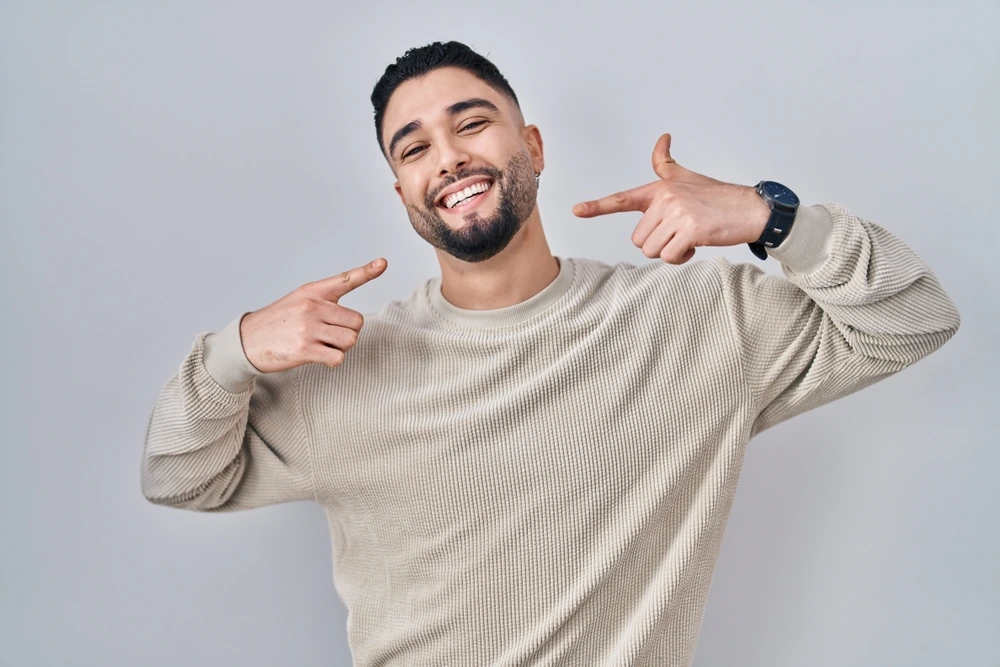 shutterstock_2185565295 A smiling man pointing toward his smile